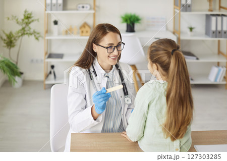 Smiling woman doctor with spatula asks child to open mouth for throat examination 127303285