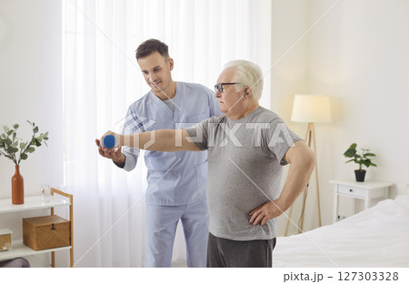 Elderly man doing exercise with dumbbell with help of professional physiotherapist 127303328