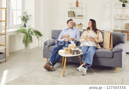 Couple resting after a lunch delivered by delivery service sitting on sofa at home. 127303358