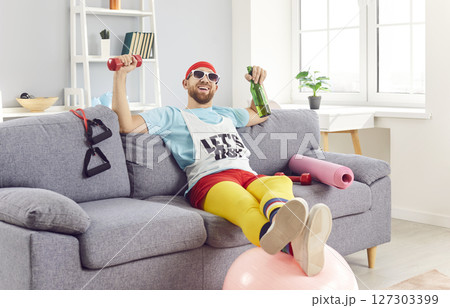 Funny cute happy sportsman sitting at home on sofa to relax after sport, playful fitness comedian Funny cute happy sportsman sitting at home on sofa to relax after sport, playful fitness comedian 127303399
