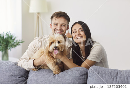 Portrait of happy laughing young couple close near couch with cute little dog, husband and wife  127303401