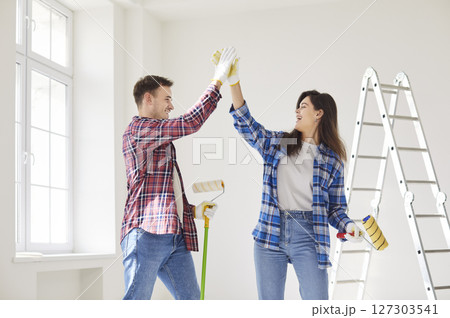 Happy couple giving high five while painting the wall of their new apartment holding paint rollers. 127303541