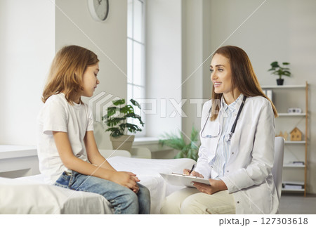 Friendly female pediatrician talking with little boy patient sitting on couch in medical clinic Friendly female pediatrician talking with little boy patient sitting on couch in medical clinic 127303618