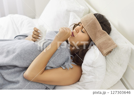 Sick young woman lying on bed at home with seasonal flu or cold feeling unhealthy with influenza 127303646