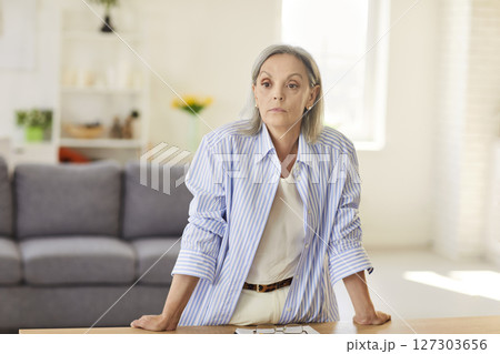 Serious Elderly Woman Standing In Home Office With Focused Expression 127303656