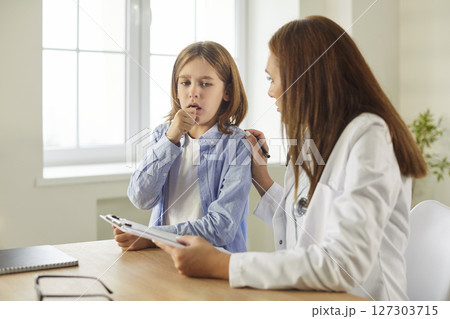 Pediatrician talking with boy patient suffering from cough sitting in office during medical exam 127303715