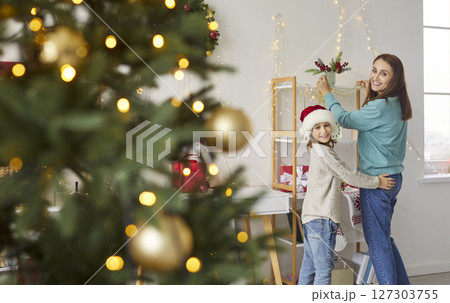 Happy mother and child decorating living room at home with Christmas tree on foreground Happy mother and child decorating living room at home with Christmas tree on foreground 127303755