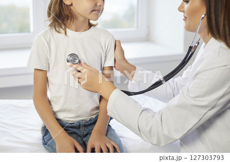 Caring kind woman doctor holding stethoscope listening to small boy patient heart chest in hospital Caring kind woman doctor holding stethoscope listening to small boy patient heart chest in hospital 127303793