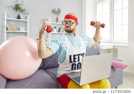 Funny sportsman doing online exercise with laptop, dumbbell weight training at home  127303800