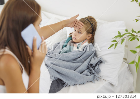 Mother Calling A Doctor For Sick Son At Home Using A Phone 127303814