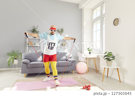 Funny young man in sportswear having home workout doing stretching exercise with rubber band. Funny young man in sportswear having home workout doing stretching exercise with rubber band. 127303845