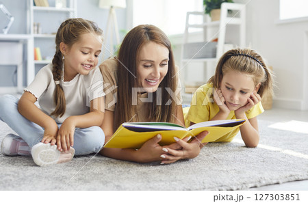 Young mother reading a book with her two little cute children lying on floor in living room at home Young mother reading a book with her two little cute children lying on floor in living room at home 127303851