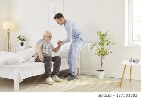 Doctor Or Nurse Assisting Elderly Patient Out Of Bed In Morning At Nursing Home Doctor Or Nurse Assisting Elderly Patient Out Of Bed In Morning At Nursing Home 127303882