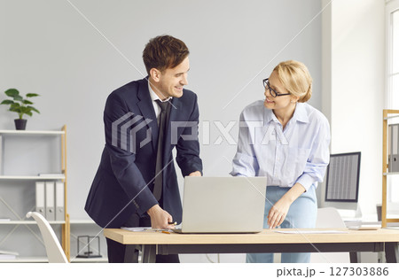 Two company employees standing in office, working together in collaborative project, using laptop. Two company employees standing in office, working together in collaborative project, using laptop. 127303886
