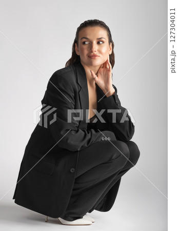 Studio portrait of beautiful woman with black suit and wet hair squatting on floor 127304011