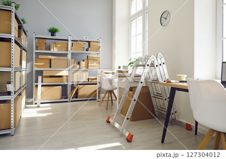 Empty space with office desk in warehouse with shelves filled cardboard boxes of retail products 127304012