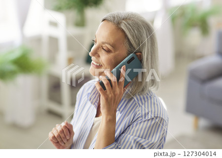 Senior happy mature woman retired engaged in pleasant talk on phone holding gadget close to ear 127304014
