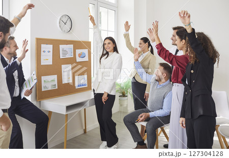 Young cheerful company employees raising hands to vote at the conference standing in meeting room. Young cheerful company employees raising hands to vote at the conference standing in meeting room. 127304128