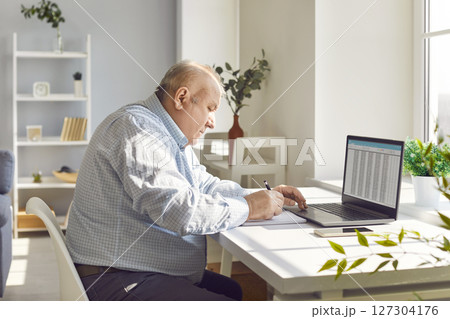 Old senior man working using laptop with chart sitting at the desk at home 127304176