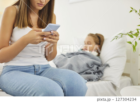 Mother Using A Phone To Search For Information About Son Illness At Home 127304234