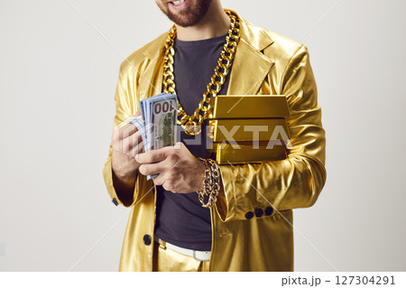 Man in funny golden suit holding gold bar and counting cash dollar banknotes Man in funny golden suit holding gold bar and counting cash dollar banknotes 127304291