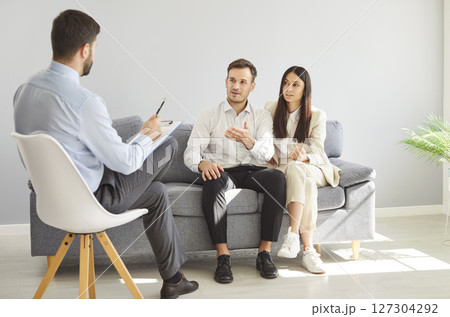 Couple sitting with psychologist and talking about marriage problems during therapy session 127304292