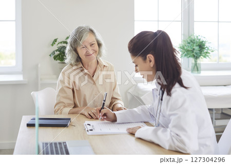 Physician writing out a prescription for her happy, smiling, senior woman patient 127304296