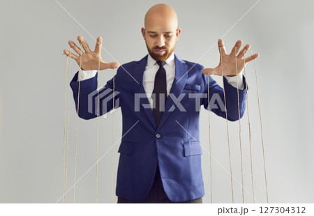 Man in suit pulling strings of puppet. 127304312