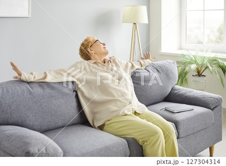 Mature peaceful woman in casual clothes sitting on comfortable sofa resting at home Mature peaceful woman in casual clothes sitting on comfortable sofa resting at home 127304314
