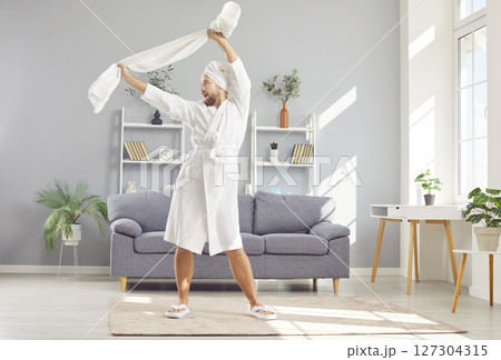 Happy, funny man in a white bathrobe and towel relaxing and having fun after shower Happy, funny man in a white bathrobe and towel relaxing and having fun after shower 127304315