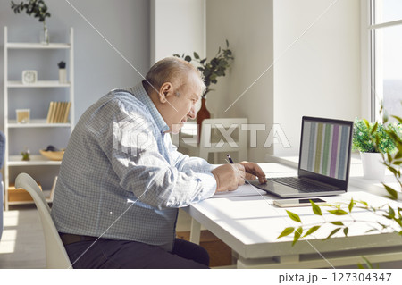 Old senior man accountant working using laptop with chart sitting at desk at home Old senior man accountant working using laptop with chart sitting at desk at home 127304347