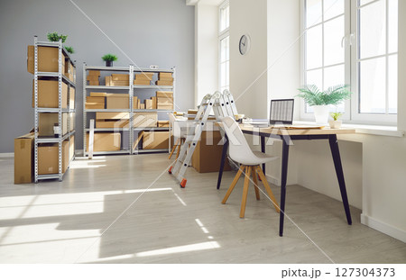 Empty space with office desk in warehouse with shelves filled cardboard boxes of retail products Empty space with office desk in warehouse with shelves filled cardboard boxes of retail products 127304373
