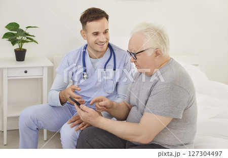 Young physician and senior patient using health care application on mobile phone 127304497
