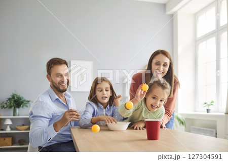 Happy young family playing together in living room at home throwing balls into cardboard cup 127304591