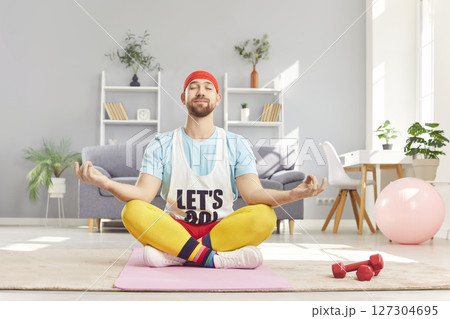 Relaxed peaceful funny young man doing yoga exercise sitting on the floor in lotus pose. 127304695