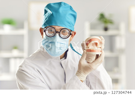 Close up of funny man doctor dentist looking at camera holding jaws standing in dentistry clinic. 127304744