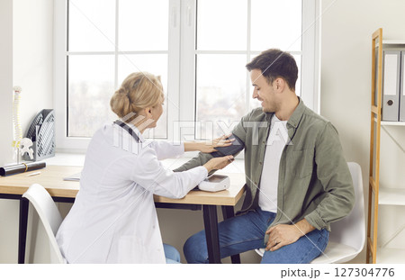 Female doctor therapist measuring blood pressure of male patient in medical clinic. 127304776
