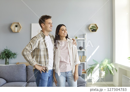 Young happy smiling couple standing in living room at home and looking at window together 127304783