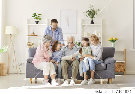 Big happy family sitting on sofa at home looking through a photo album enjoying good memories 127304874