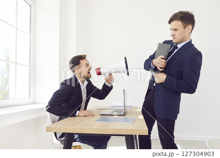 Angry boss holding mouthpiece and shouting at stressed employee standing in office. 127304903