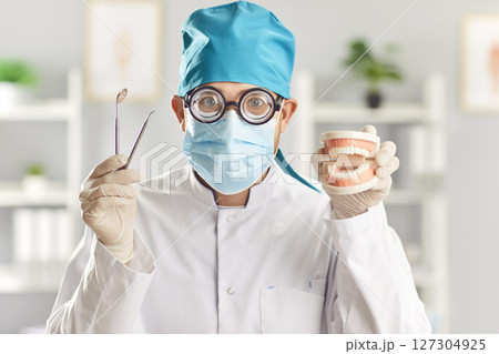 Funny doctor dentist with dental tools and jaws in medical uniform at work in dentistry clinic Funny doctor dentist with dental tools and jaws in medical uniform at work in dentistry clinic 127304925