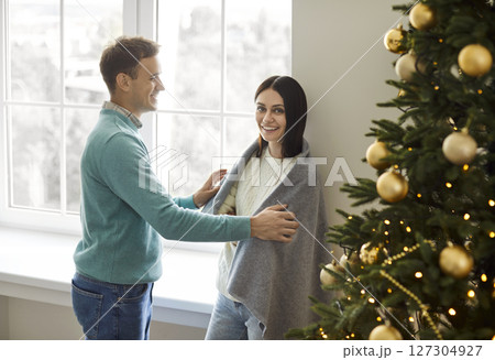 Happy young couple standing by large window and Christmas tree, enjoying festive atmosphere at home. Happy young couple standing by large window and Christmas tree, enjoying festive atmosphere at home. 127304927
