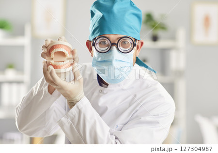 Funny man doctor dentist looking at camera holding jaws standing in dentistry clinic. Funny man doctor dentist looking at camera holding jaws standing in dentistry clinic. 127304987