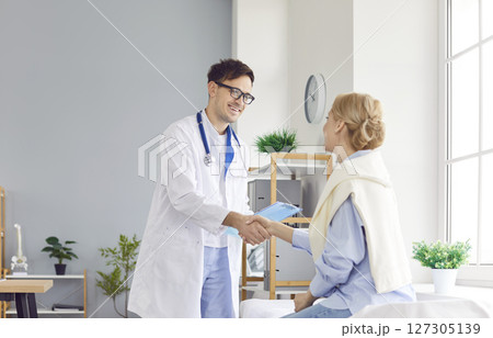 Happy Doctor Or Nurse Shaking Hands With Patient In Hospital Office 127305139