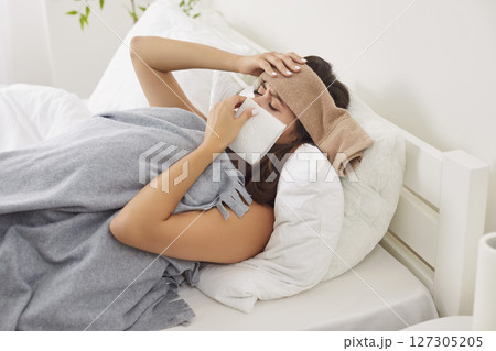 Sick young woman with fever lying in bed, sneezing in tissue, suffering from cold, infection or flu. Sick young woman with fever lying in bed, sneezing in tissue, suffering from cold, infection or flu. 127305205