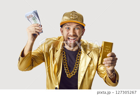 Funny young man in golden suit holding money cash and gold bar on white studio background. 127305267