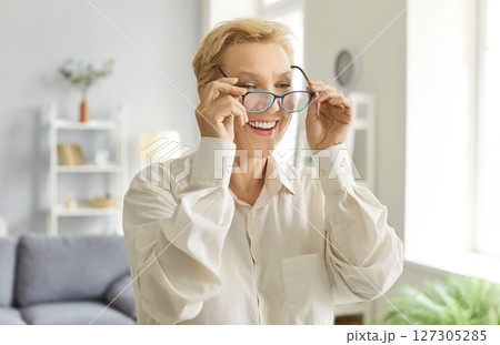 Senior woman with vision problem looking through eyeglasses standing in the living room at home 127305285