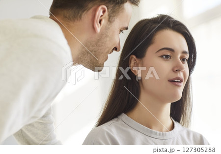 Young man whispering in the ear of brunette woman telling her secret or gossip sharing news 127305288