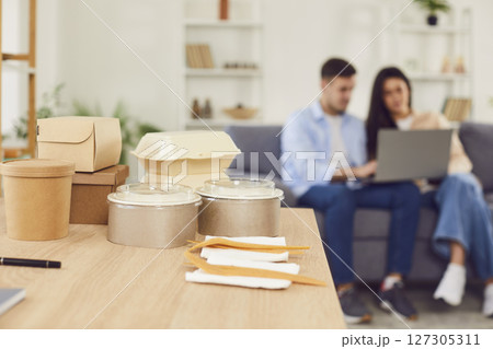 Table with food containers and forks from takeaway delivery, with family couple in background 127305311