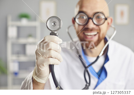 Portrait of a young funny smiling doctor in medical uniform standing with stethoscope in clinic. Portrait of a young funny smiling doctor in medical uniform standing with stethoscope in clinic. 127305337